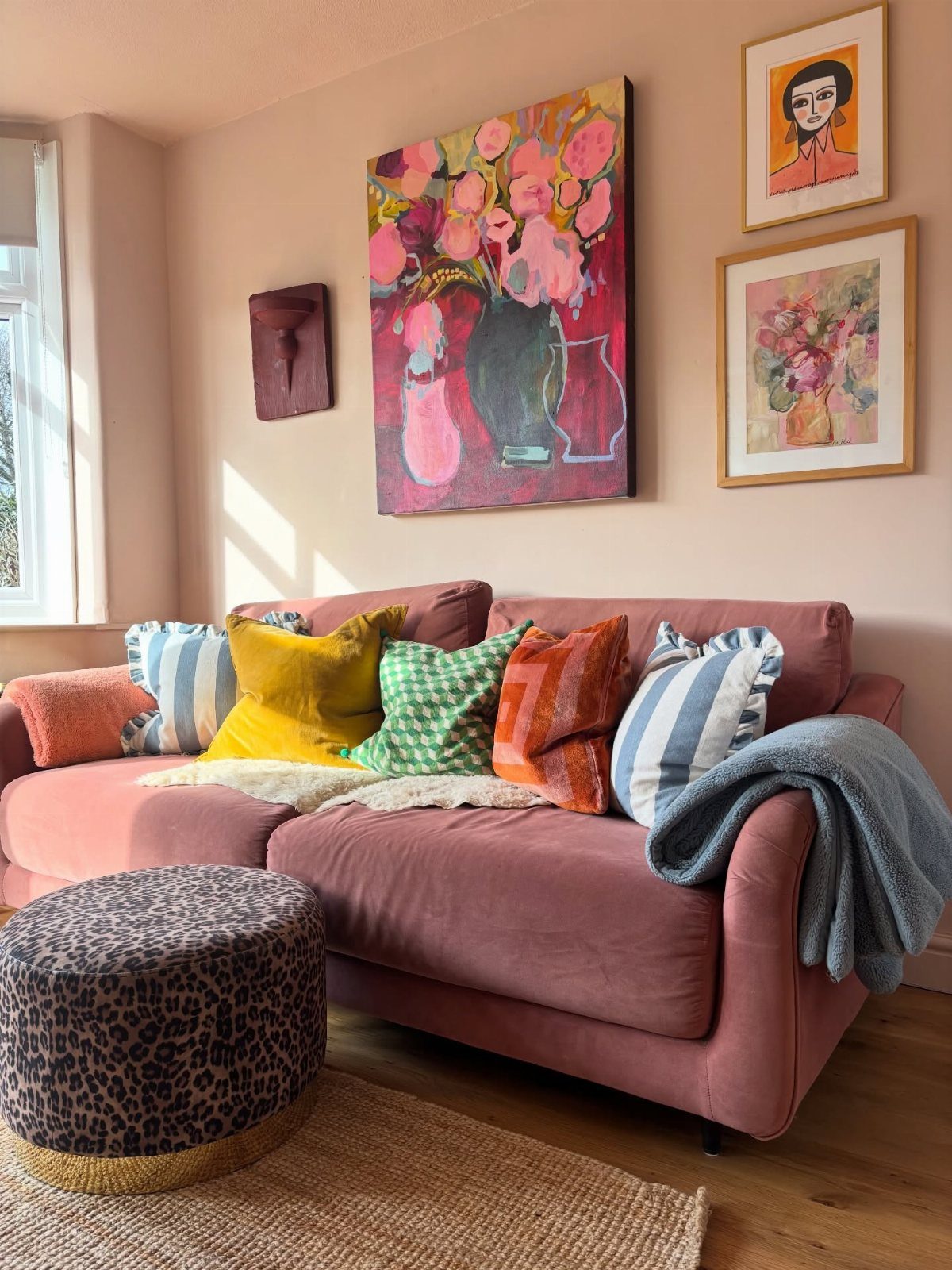 Pink sofa with colorful pillows and a large floral painting hanging above it.