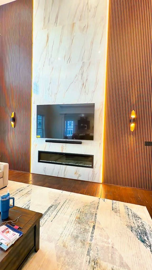 Marble focal wall with fireplace and TV flanked by wooden slat panels and lighting