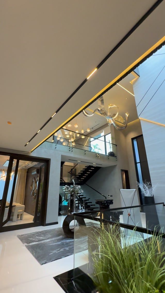 Modern high ceiling living room with a sculptural light fixture and black staircase.