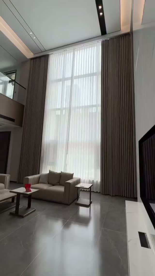 High ceiling living room with floor-to-ceiling brown curtains and a beige sofa.