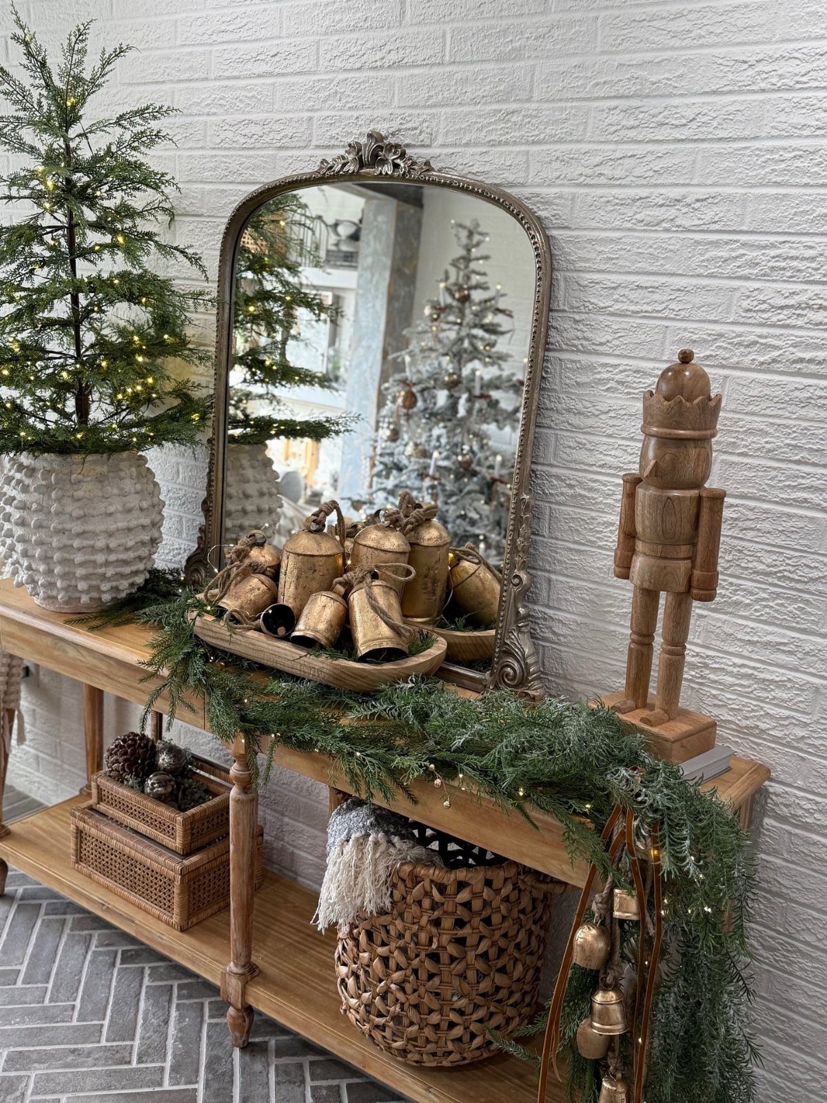Wooden console table decorated with holiday greenery, gold bells, and a nutcracker.