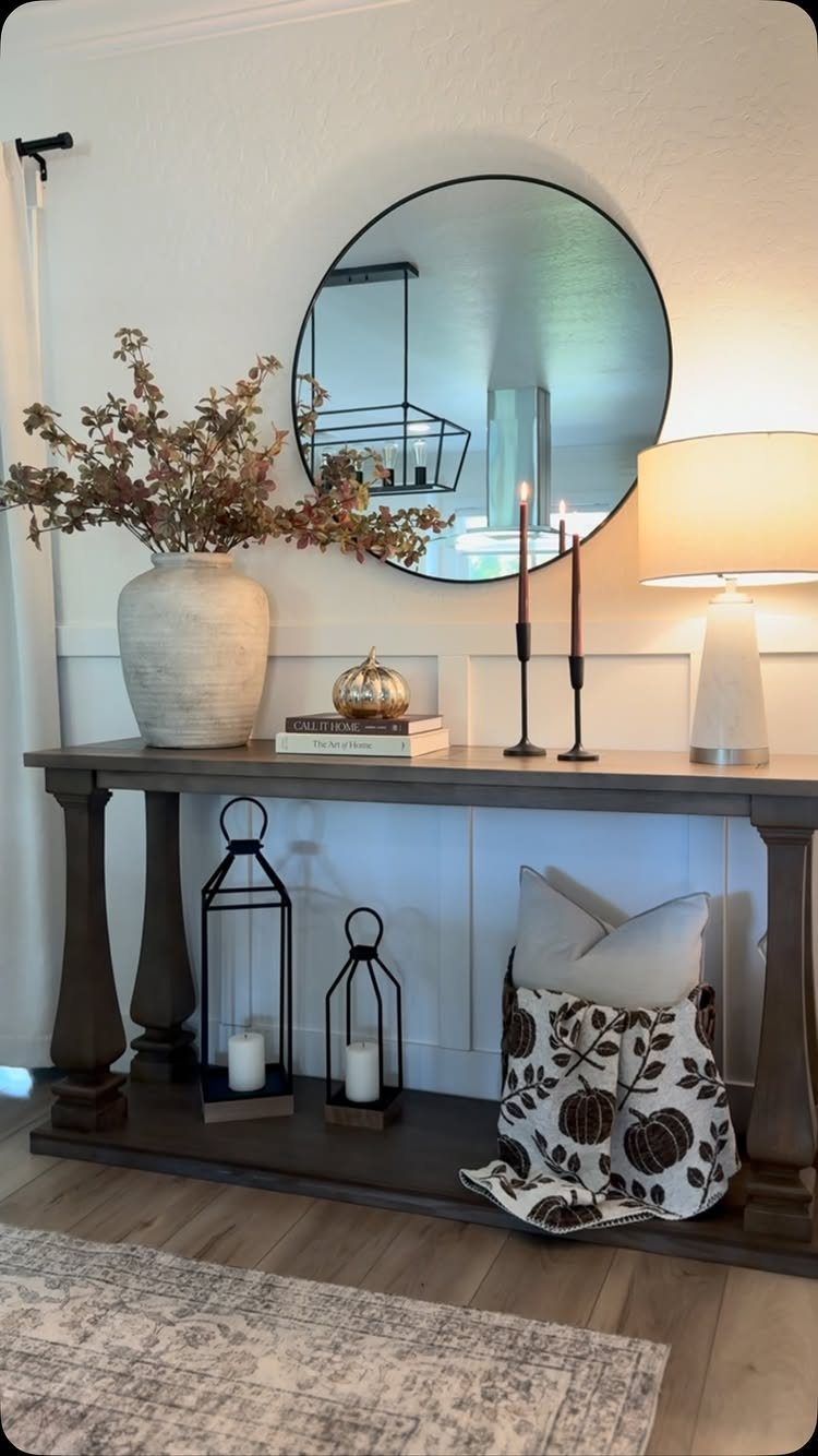 Grey console table behind a sofa decorated with books, a vase, and lamps.