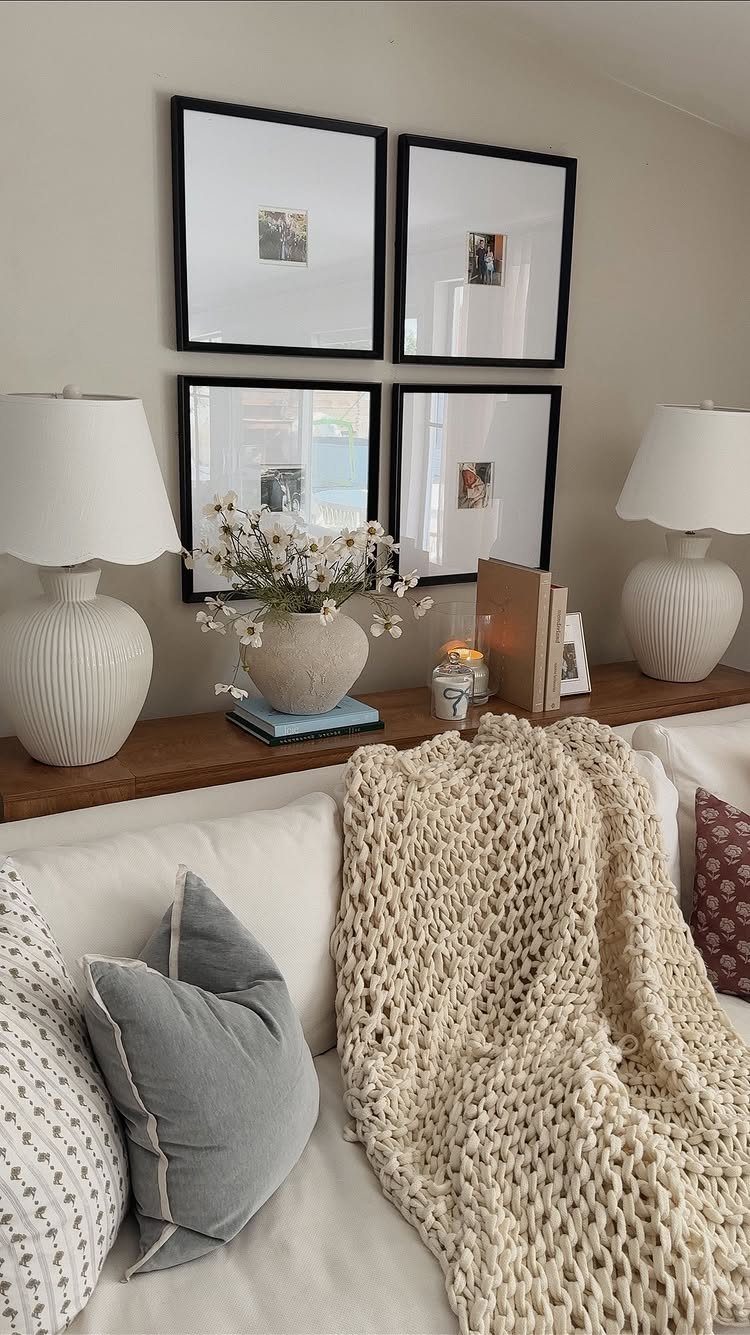 Wooden console table behind a white sofa decorated with lamps, flowers, and framed art.