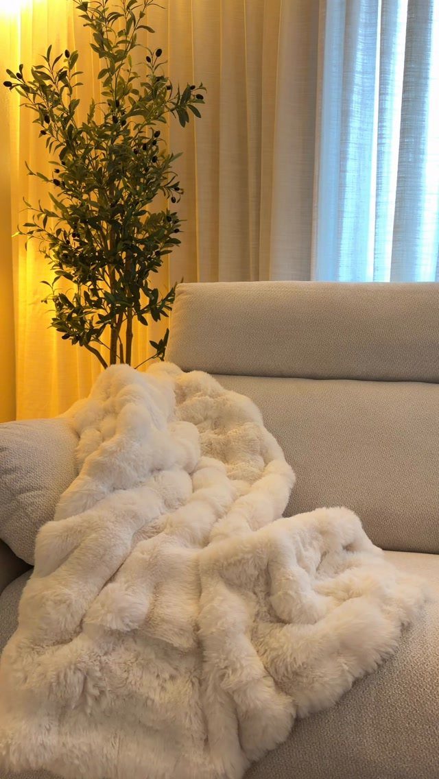 White fluffy faux-fur blanket draped over a light grey fabric sofa seat