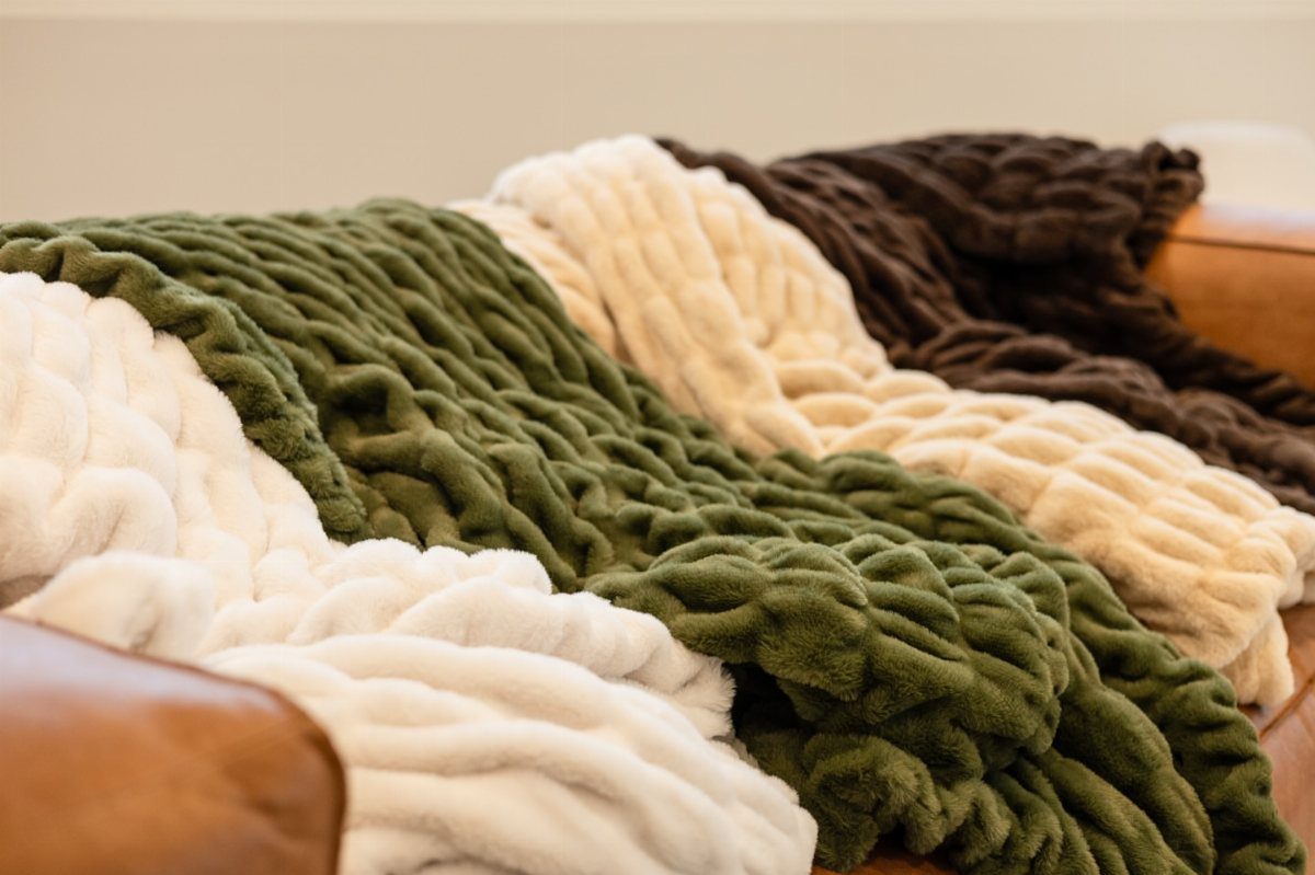 White, olive green, and brown chunky knit blankets layered on a leather sofa.