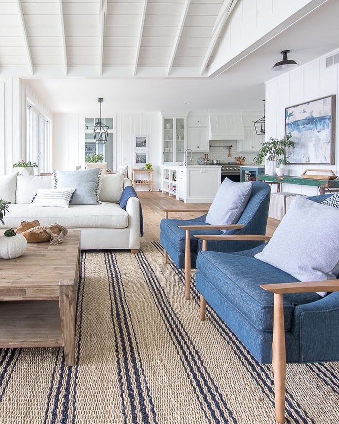 Bright living room with blue armchairs, white sofa, and striped jute rug.