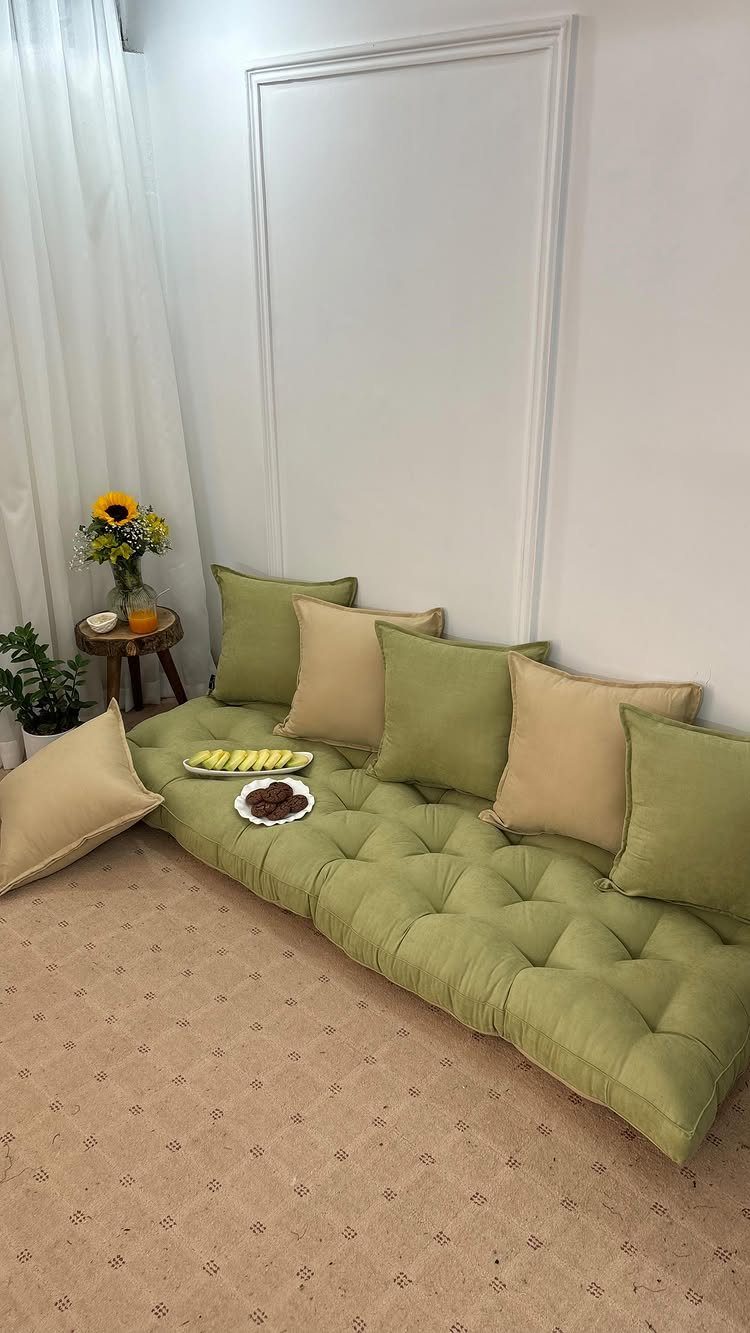 Green tufted floor seating with beige and green pillows against a white wall.