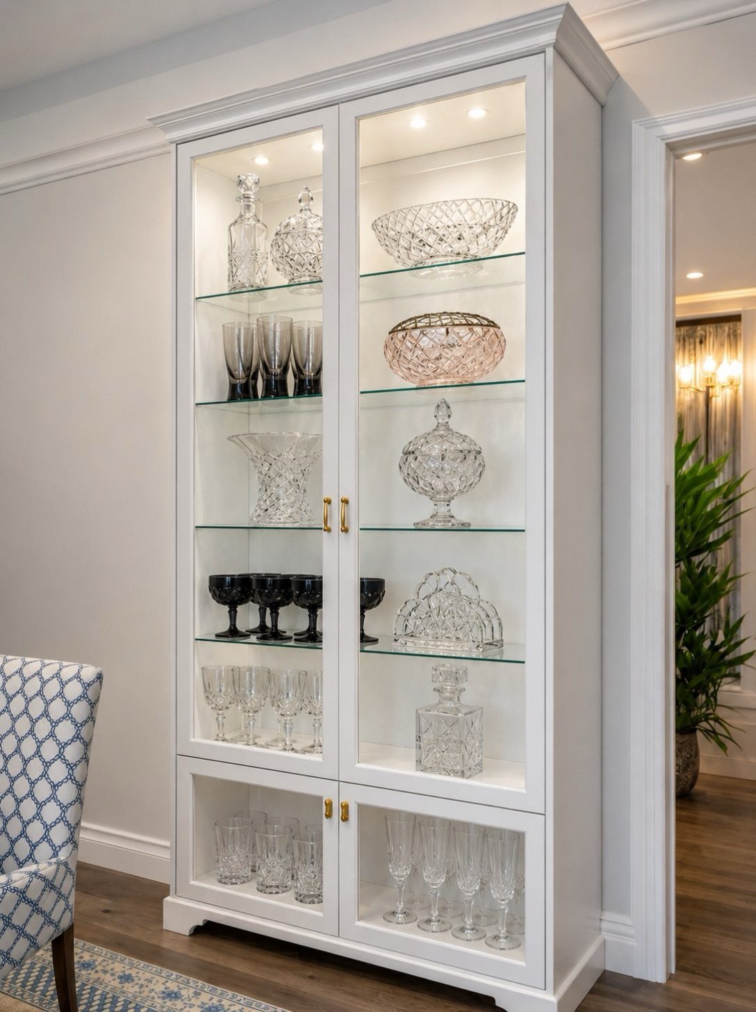 White built-in display cabinet with glass shelves holding crystal glassware and decanters.