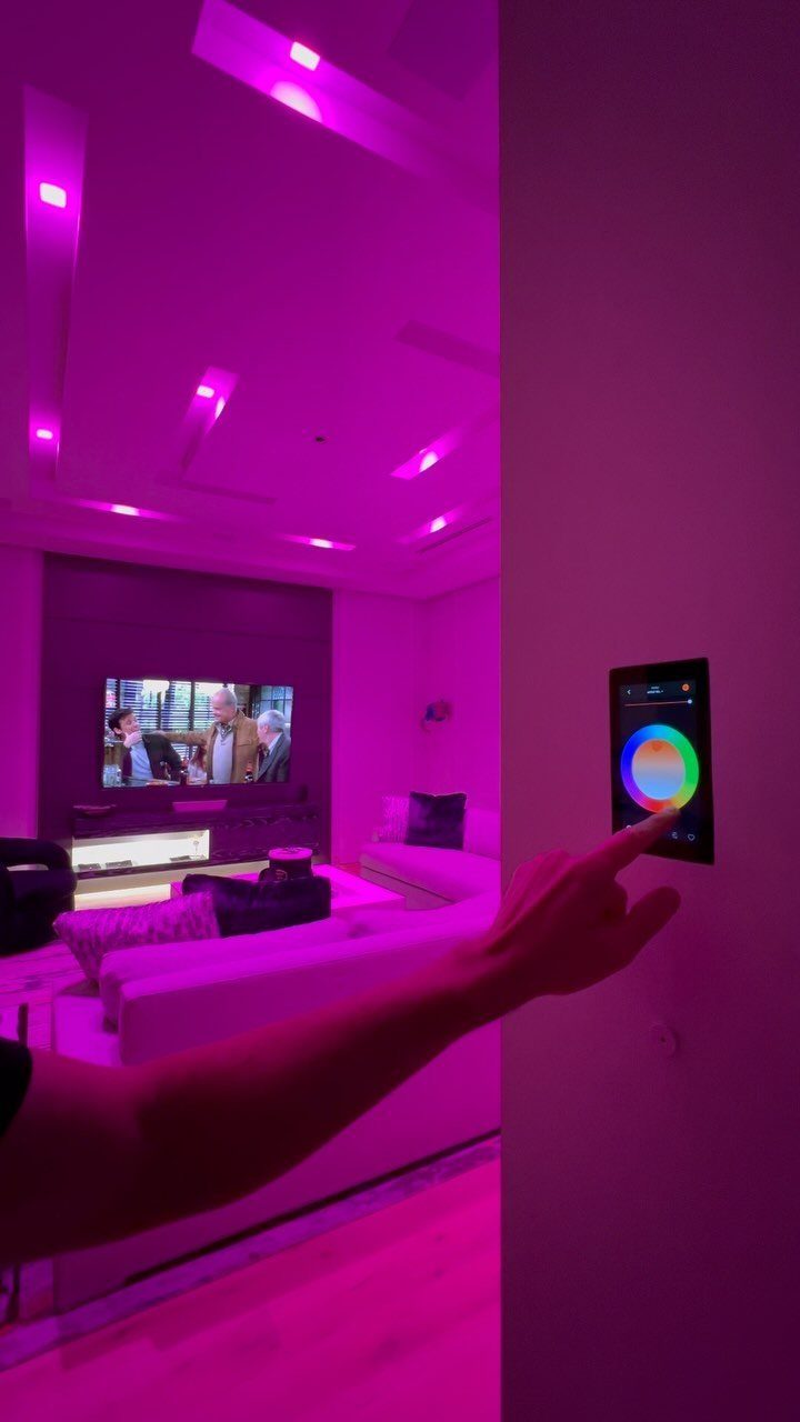 Hand adjusting a digital color wheel panel to control purple living room lighting.