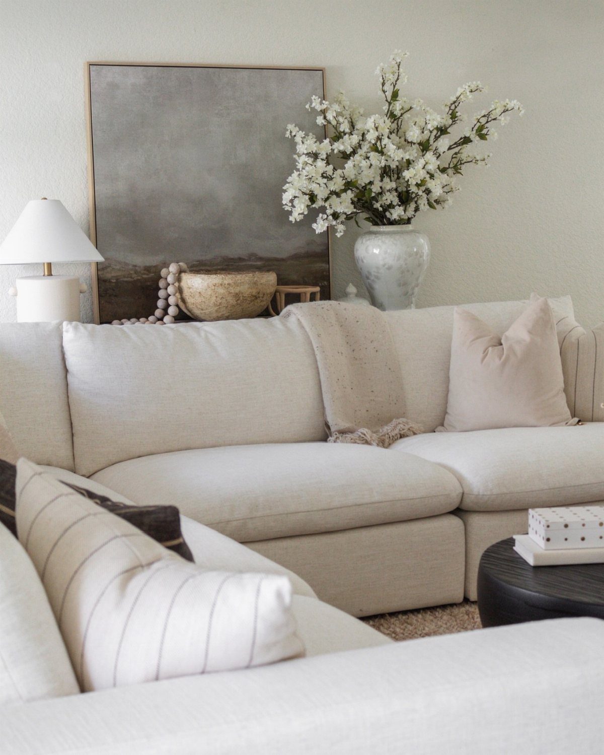 Cream fabric sofa with neutral pillows, white flowers, and abstract art in living room.