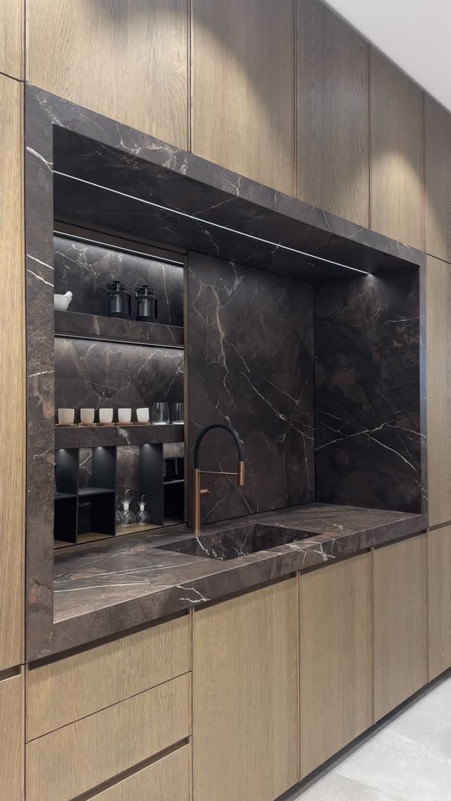 Modern built-in wet bar with dark marble surfaces and light wood cabinetry.