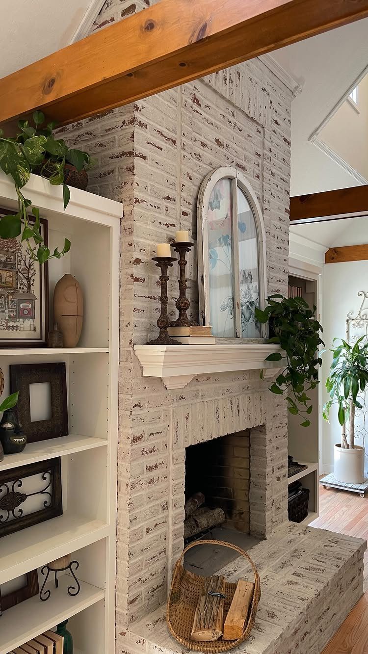 White built-in shelving unit next to a white-washed brick fireplace with wooden beams.