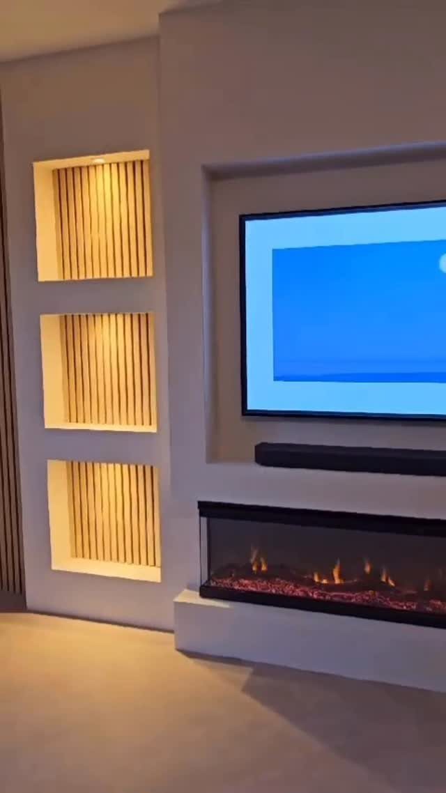 Modern living room entertainment wall with built-in niches, television, and electric fireplace.