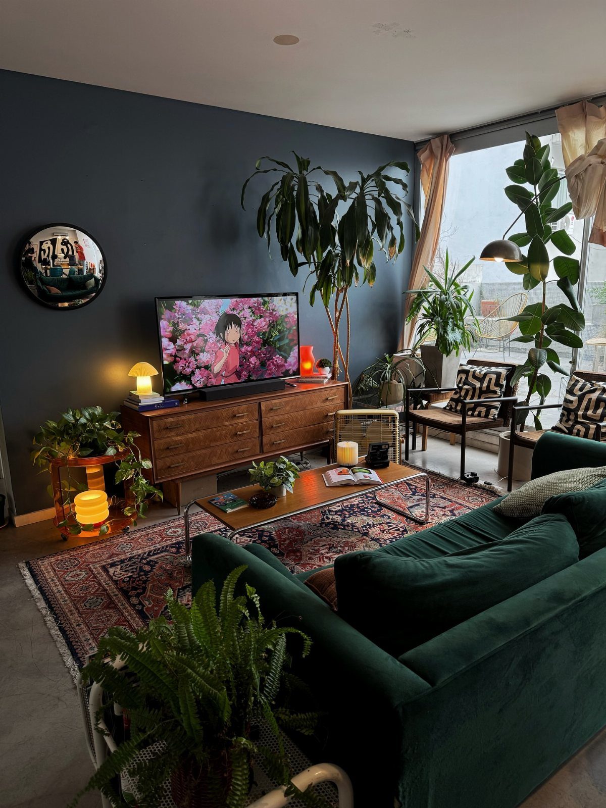 Dark charcoal wall and deep green velvet sofa in a plant-filled living room
