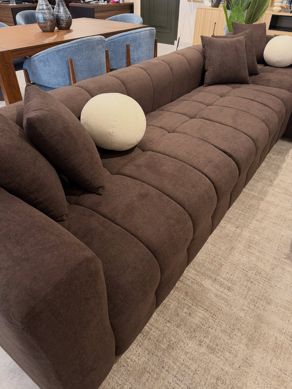 Dark brown tufted fabric sofa with cream and brown pillows on a beige rug.