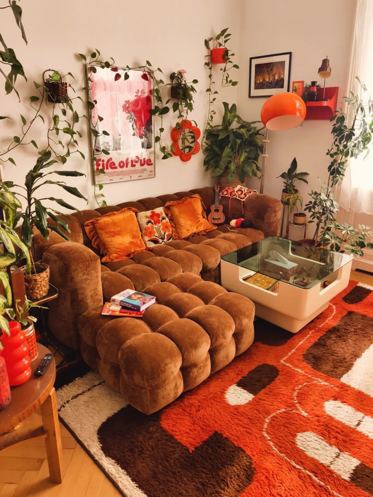 Brown tufted modular sofa with orange pillows, green plants, and a red patterned rug.