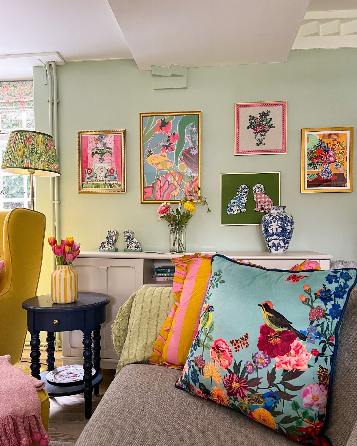 Brown sofa with colorful floral pillows against a pale green wall with art.