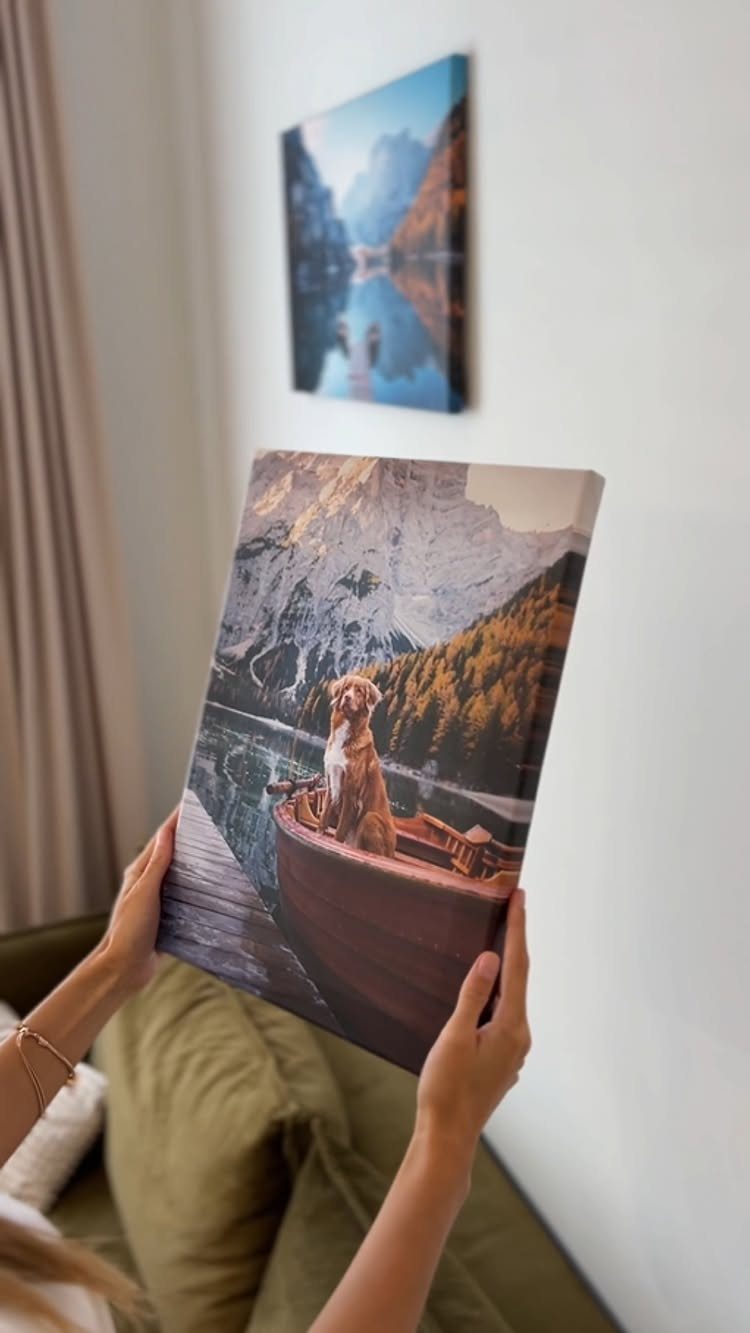 Hands holding a canvas print of a dog in a boat by mountains.