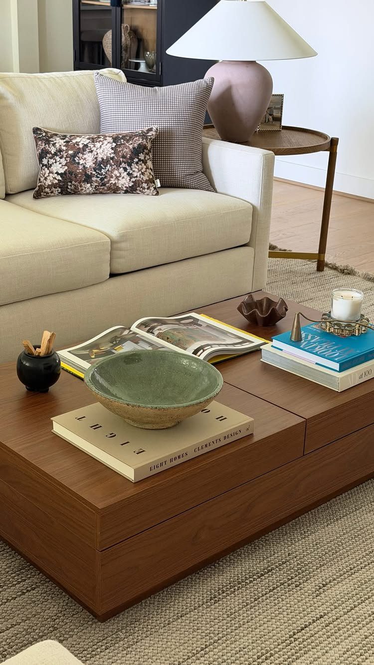 Wooden coffee table with decorative books and bowls next to a cream sofa.