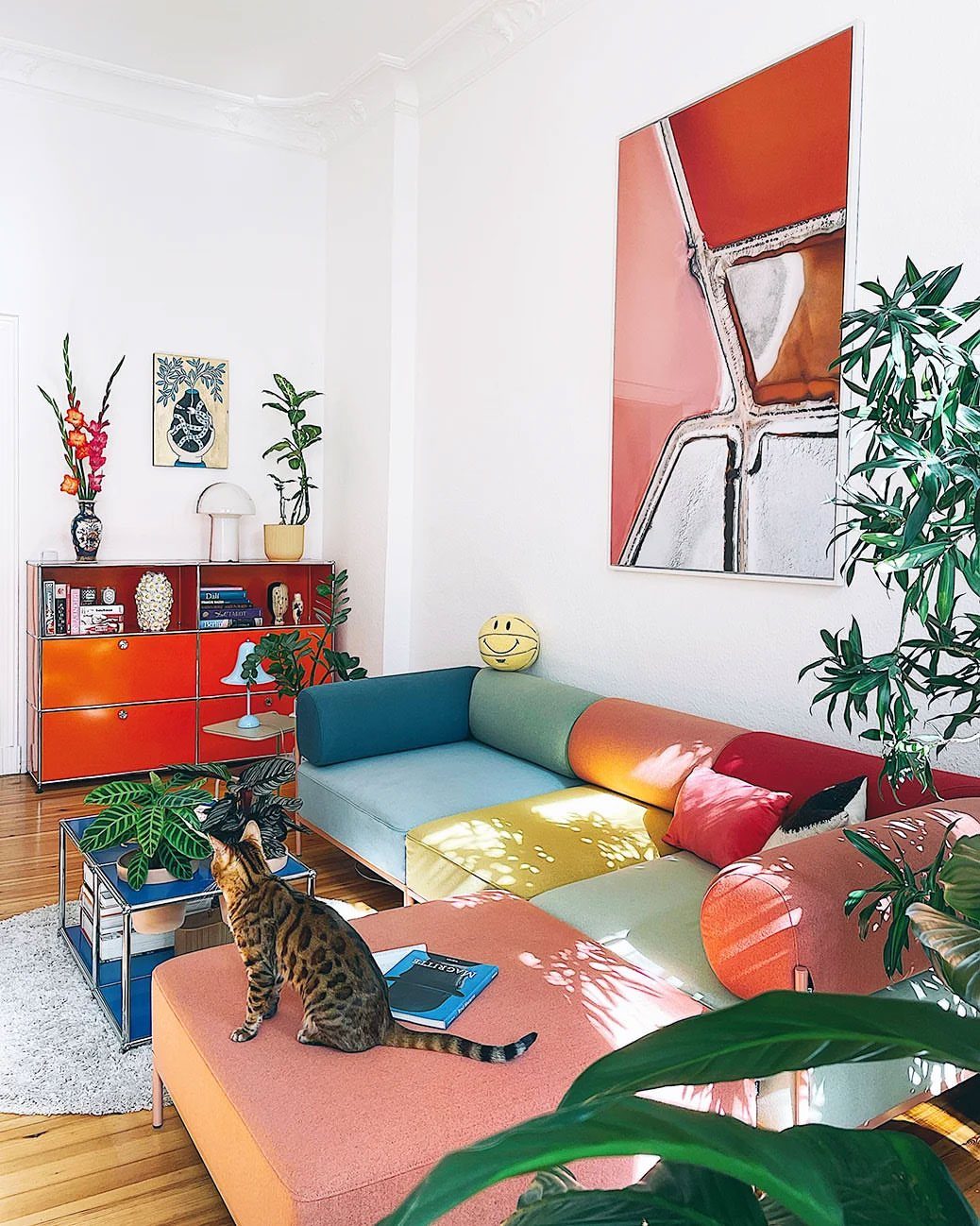 Multi-colored modular sofa and orange sideboard in a bright modern living room with art.