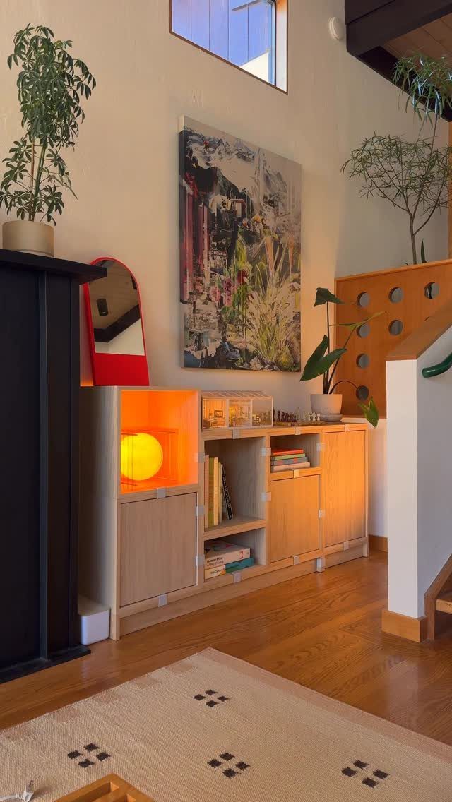Wooden modular storage unit with books and a glowing lamp in a living room.