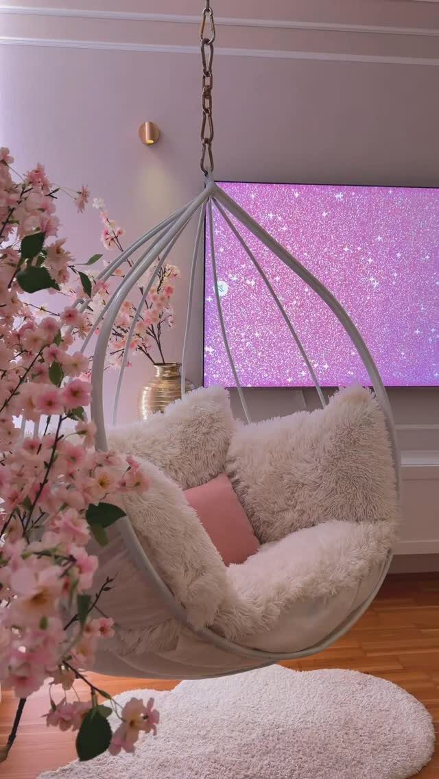 Hanging egg chair with pink and white cushions in a soft pink room.