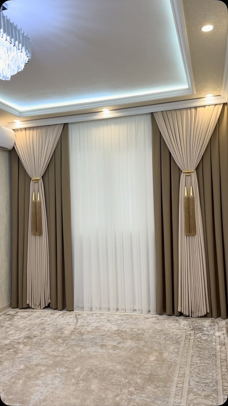 Beige and brown pleated curtains with gold tassels and sheer white inner drapes.