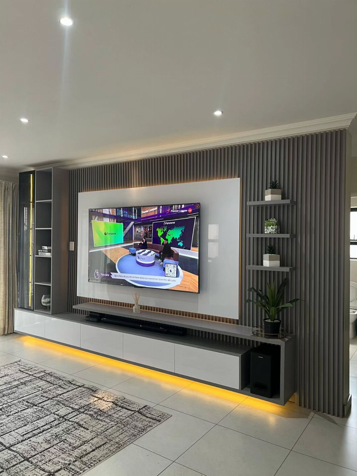 Modern living room with a large TV, grey slatted wall, and floating console.