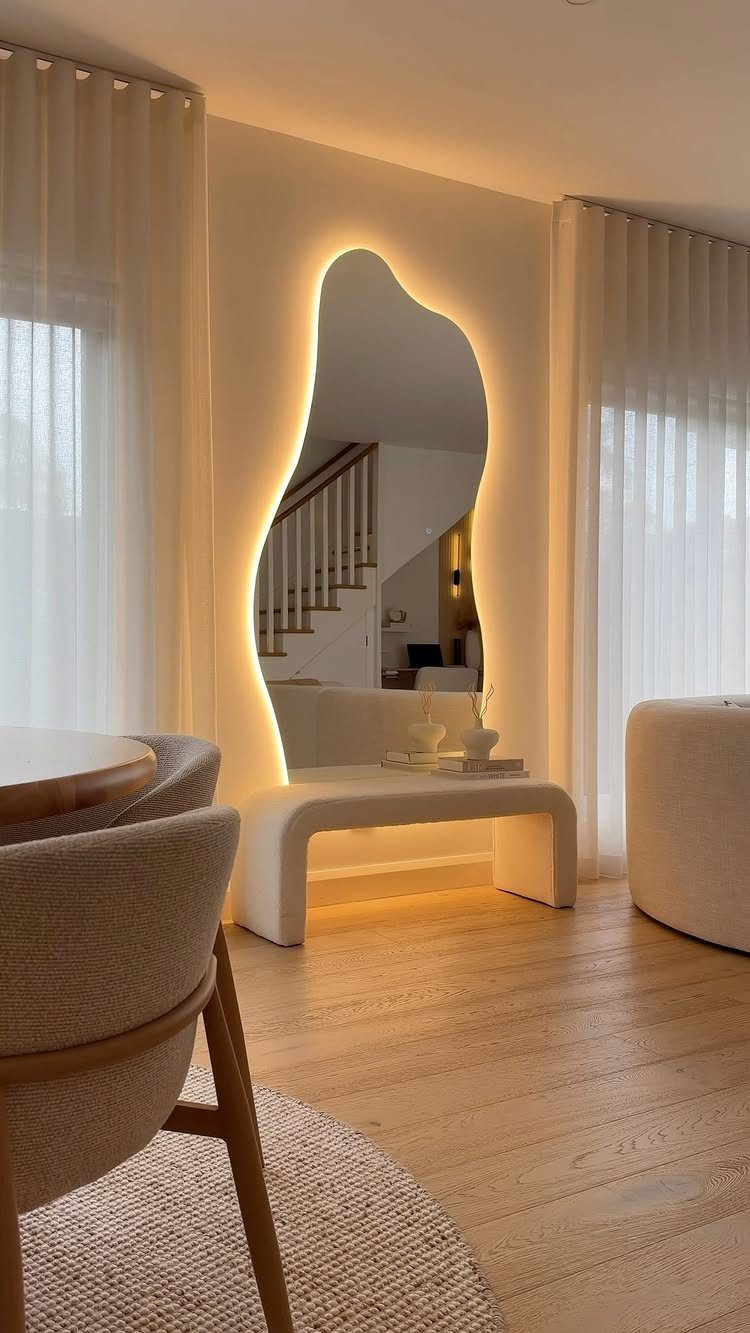 Large irregularly shaped backlit mirror leaning against a wall above a white bench.