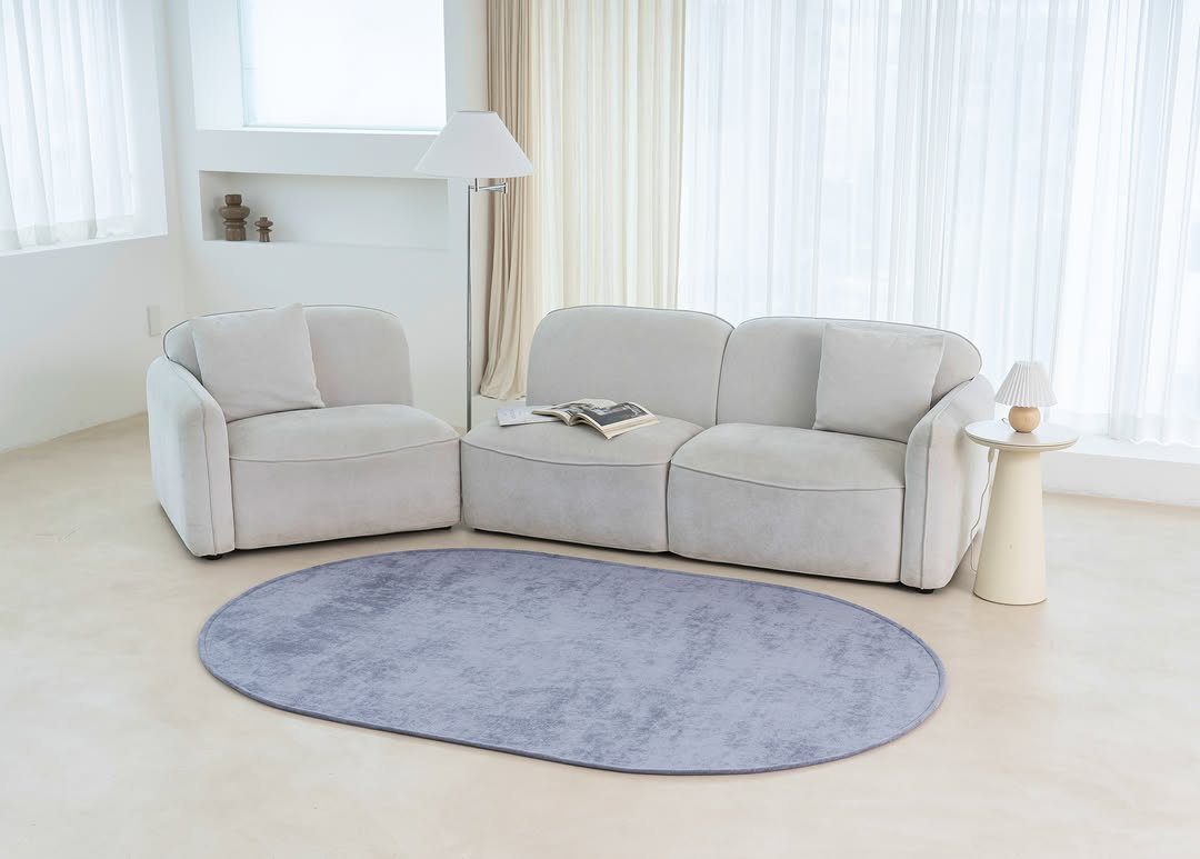 Beige curved sofa and armchair with a purple oval rug in a bright room