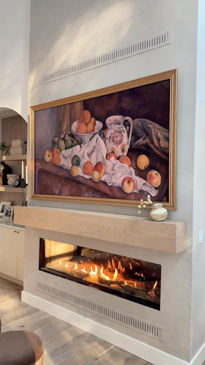 Framed still-life painting hanging above a modern linear fireplace with a wooden mantel.