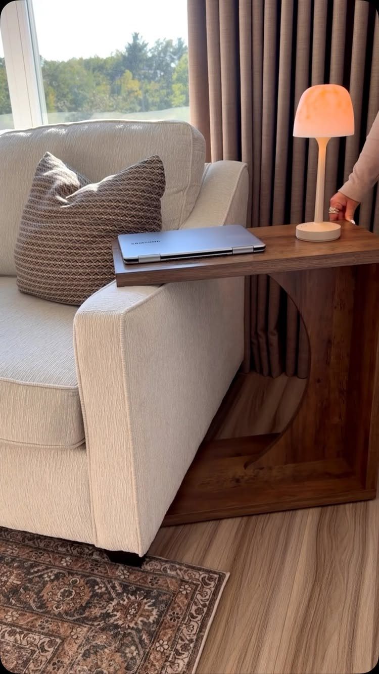 Light armchair and C-shaped wooden side table with laptop and lamp in living room