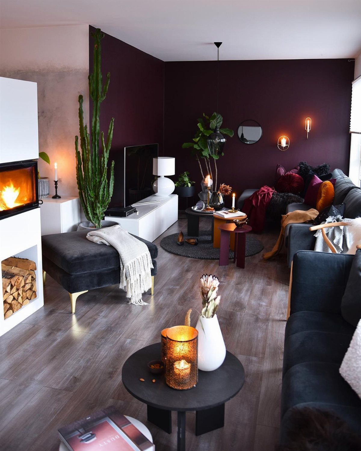 Living room with deep purple walls, dark velvet furniture, and a tall cactus.