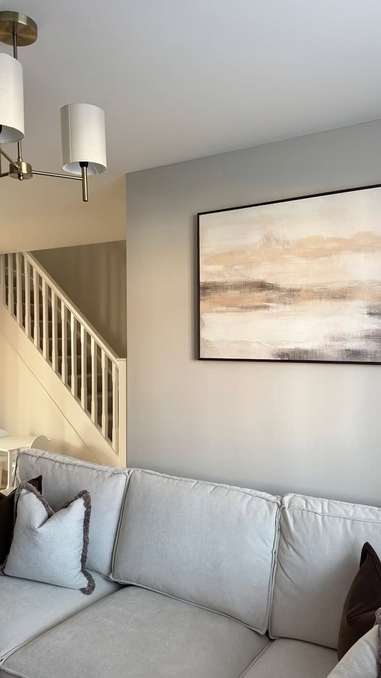 Large abstract neutral painting hanging on a grey wall above a light grey sofa.