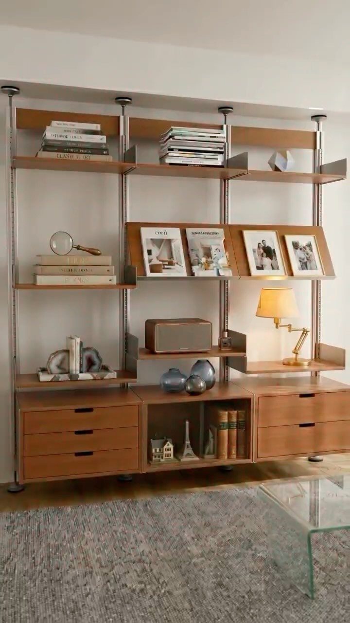 Modular wall-mounted wooden shelves and cabinets holding books, photos, and a lamp.