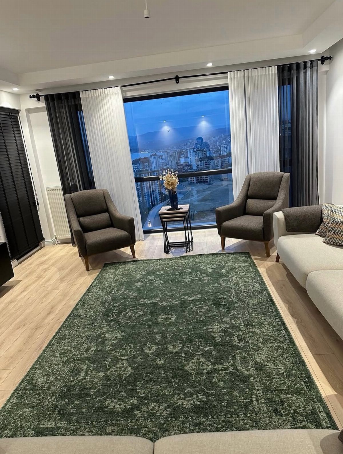 Dark green patterned rug in a modern living room with grey armchairs and city view.