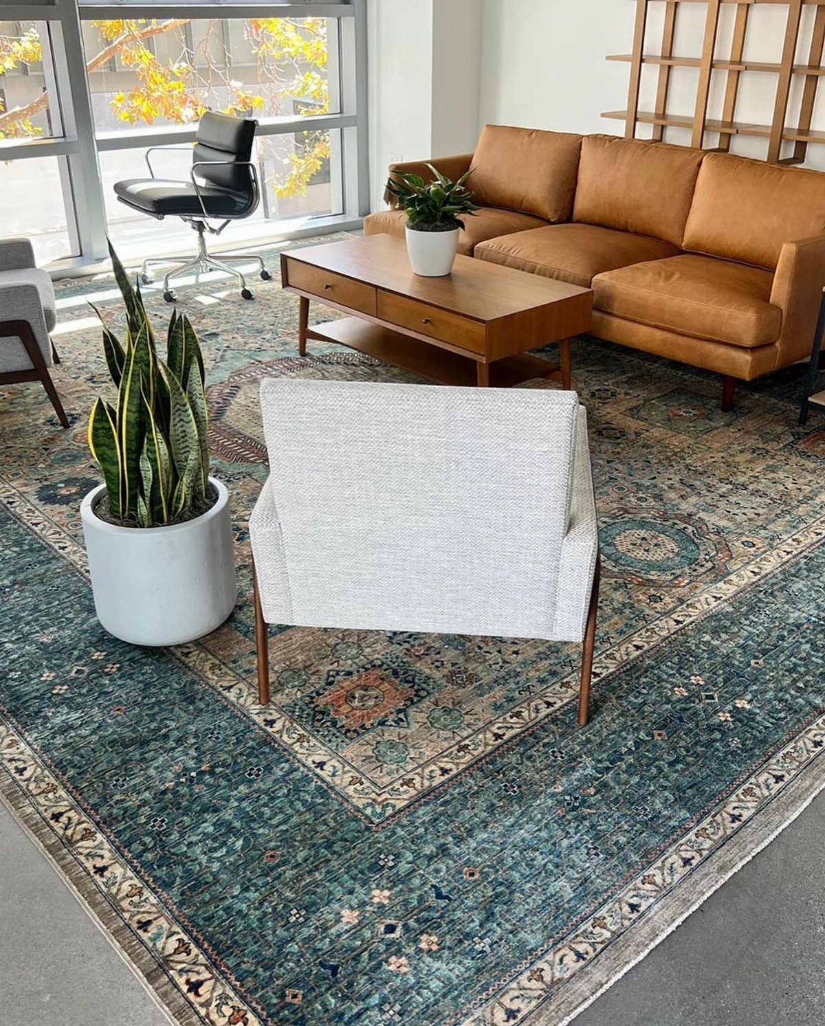 Teal and green patterned rug in a mid-century modern living room with leather sofa.