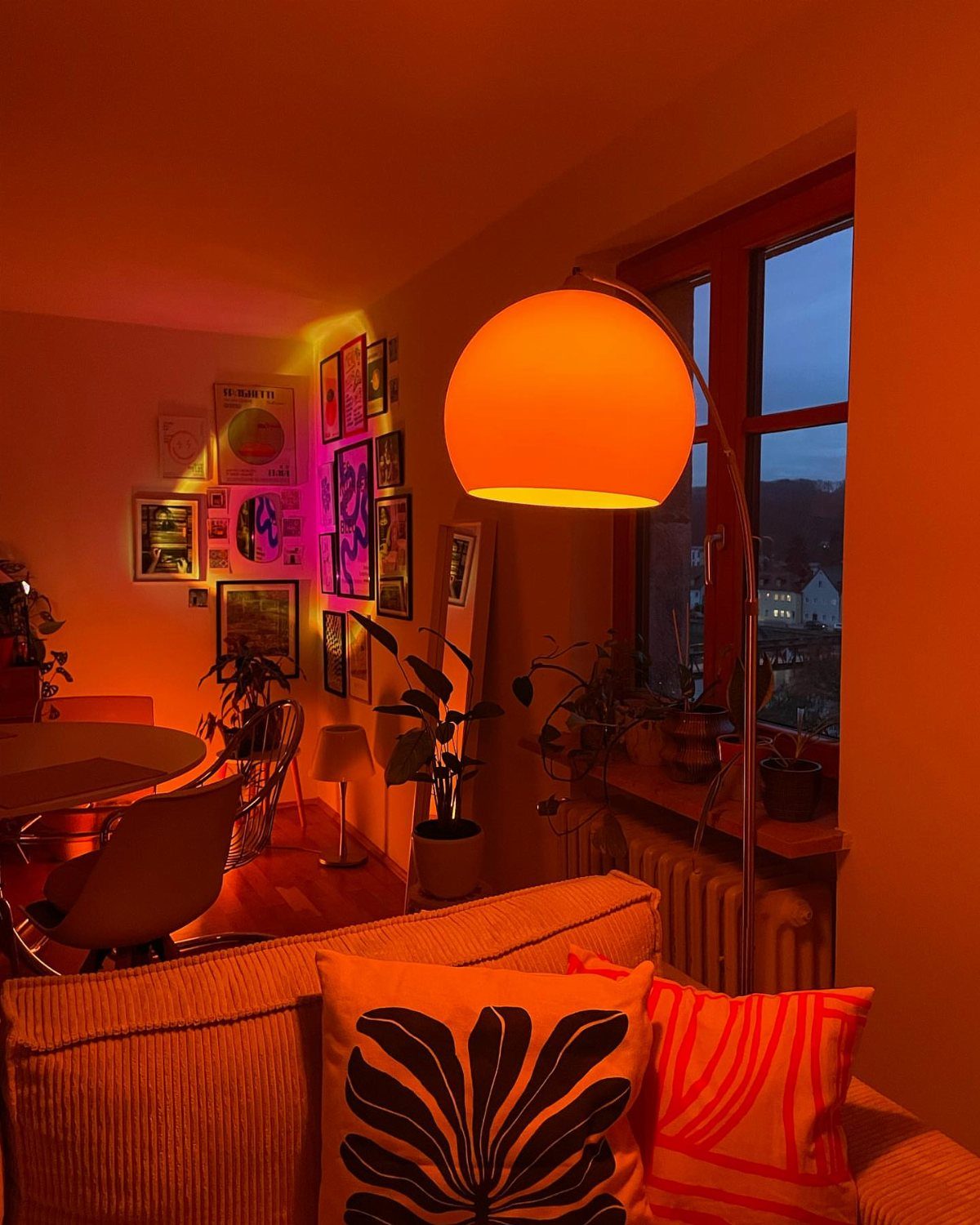 Large spherical orange arc floor lamp illuminating a cozy living room with art.