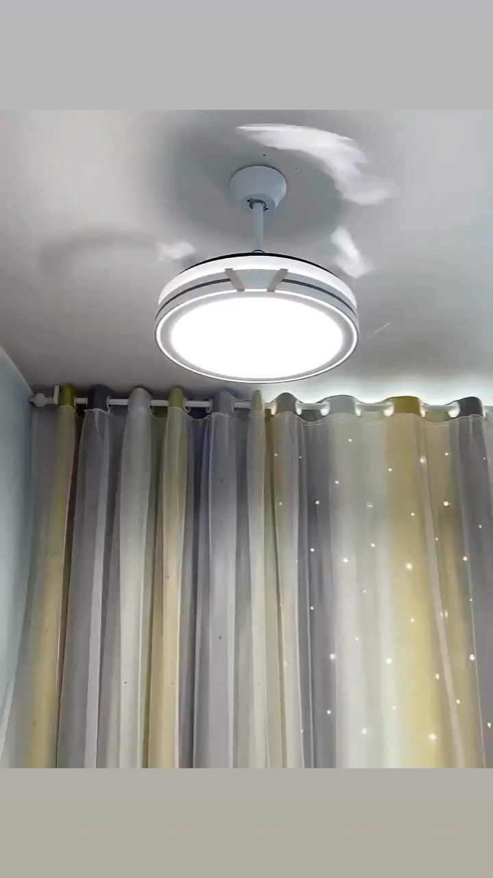 Circular white ceiling light fixture glowing brightly above grey and gold curtains.