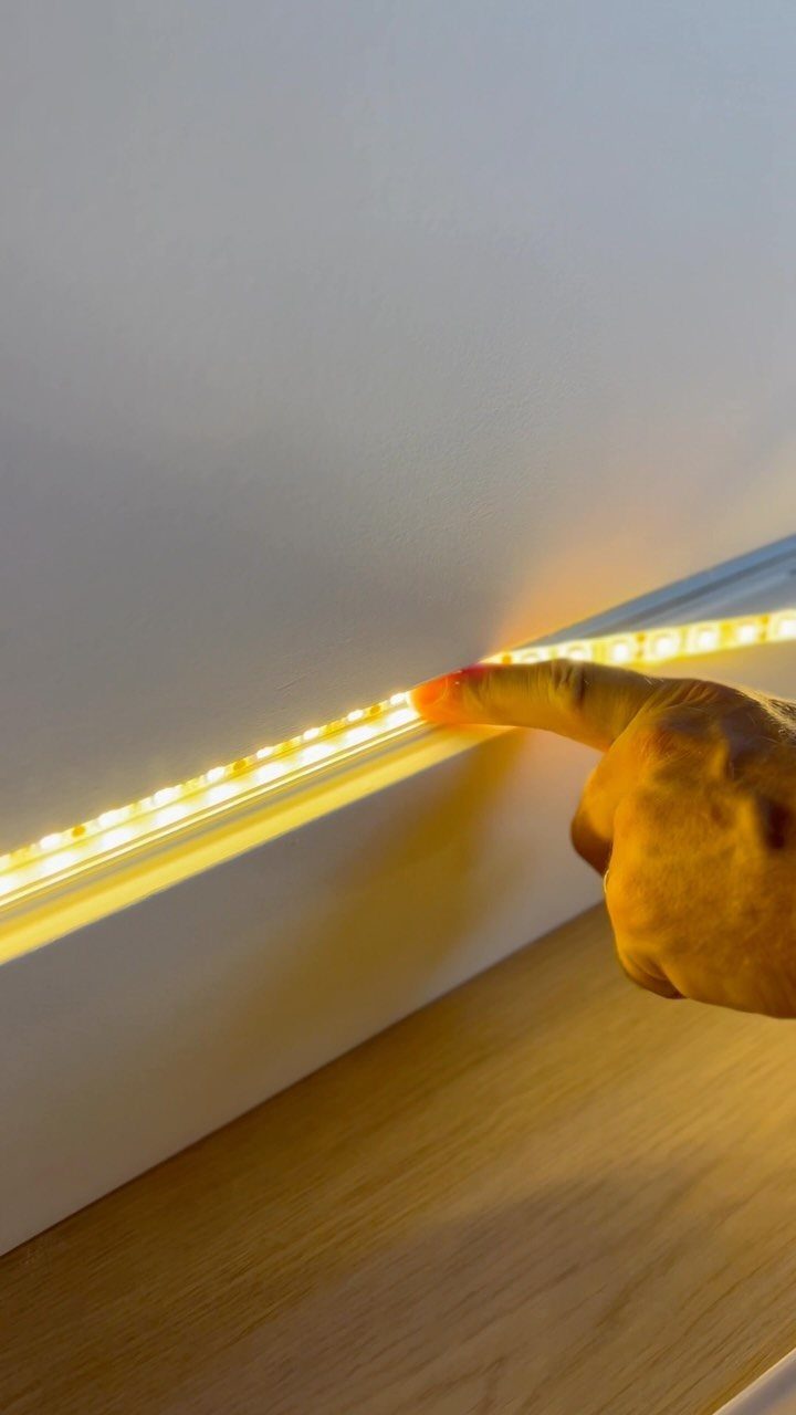 LED light strip under a white shelf being touched by a hand