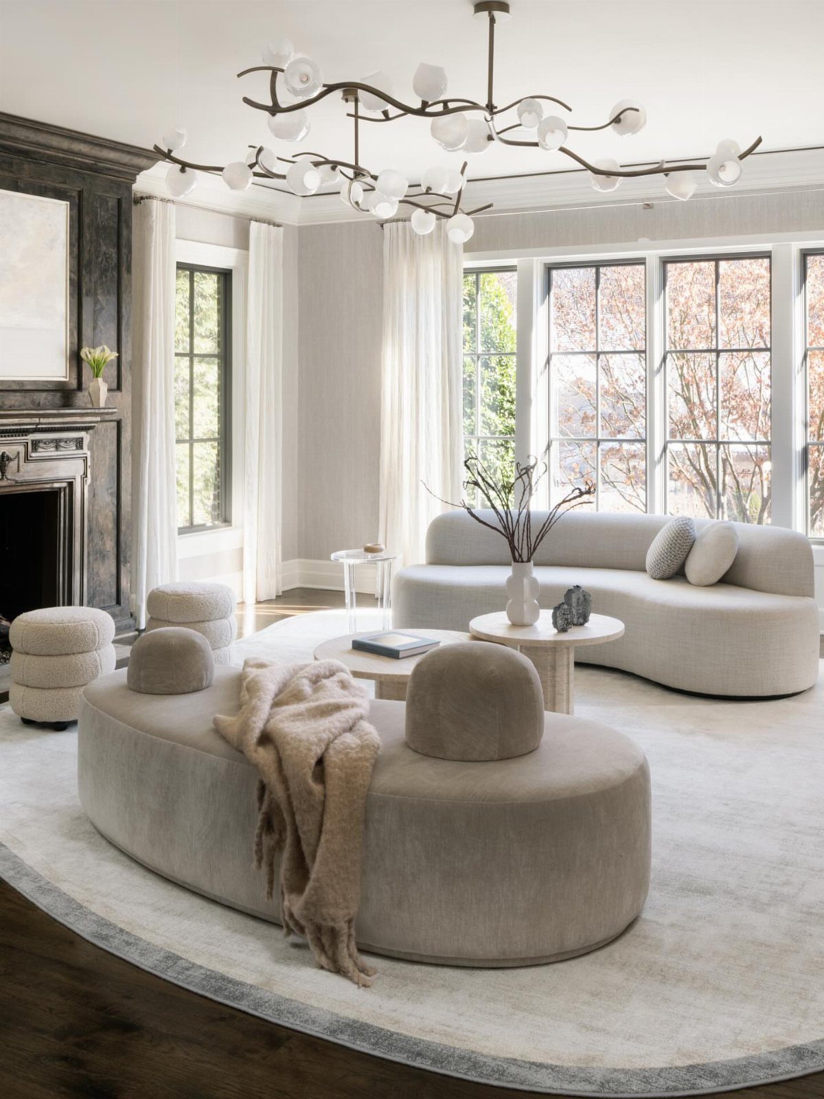 Large branch-style white chandelier hanging over a modern living room with curved furniture.