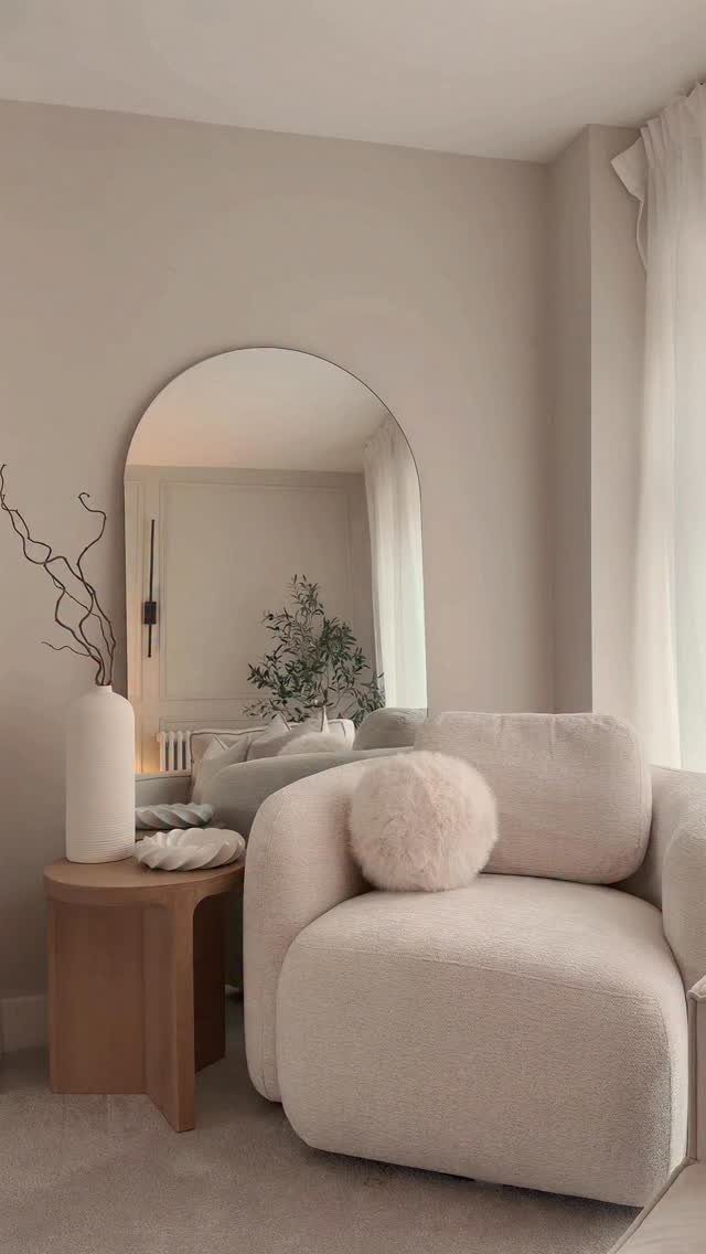 Beige living room with a curved cream armchair and large arched mirror.