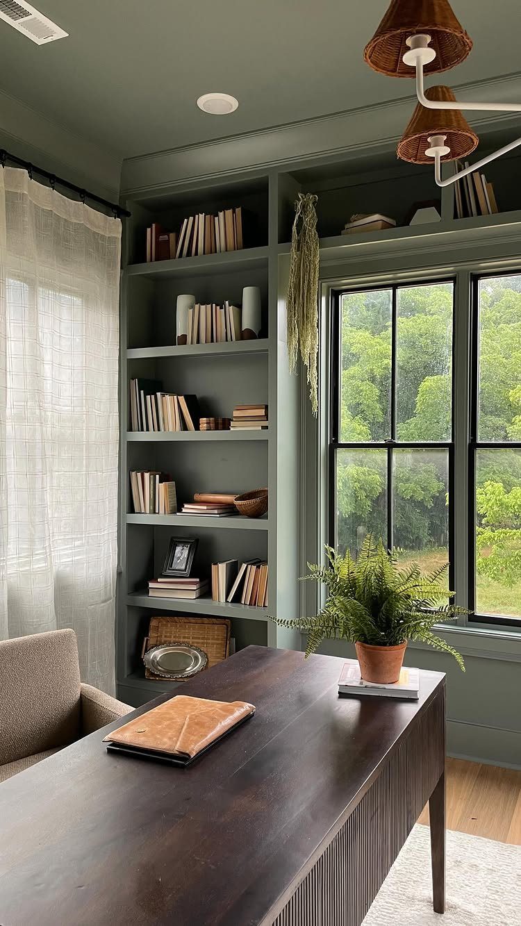 Built-in sage green shelving wrapping above and beside a large window with books.