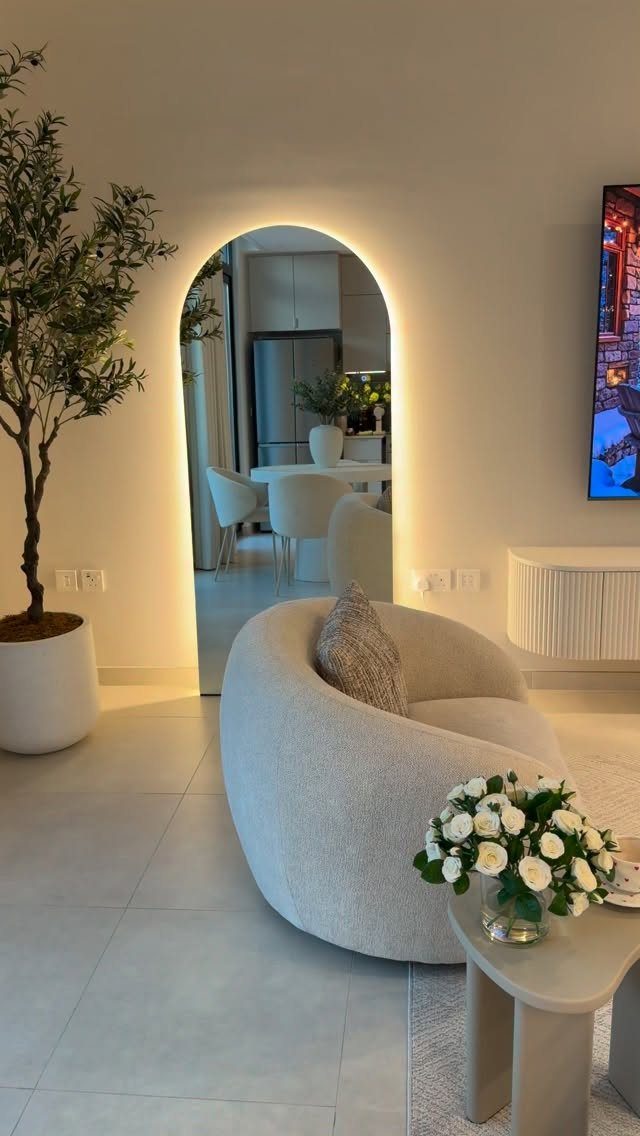 Curved white armchair and arched backlit mirror in a minimalist modern living room