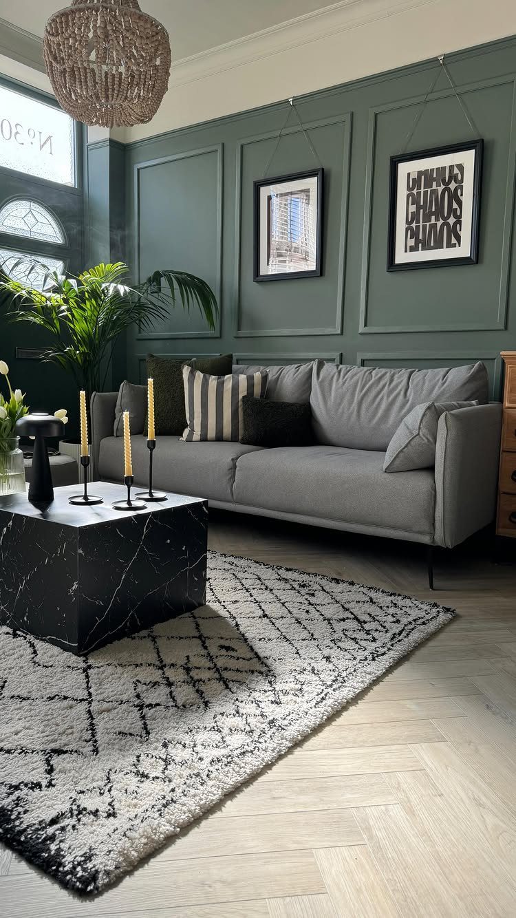 Grey sofa and black marble table in a room with green paneled walls.