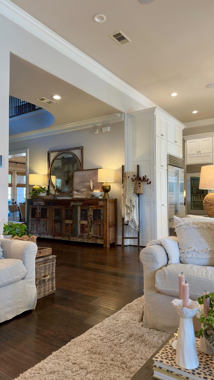Living room with white armchairs, dark wood floors, and a rustic wooden sideboard.