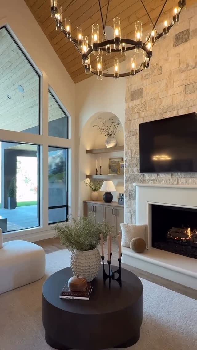 Modern living room with stone fireplace, black coffee table, and large circular chandelier.