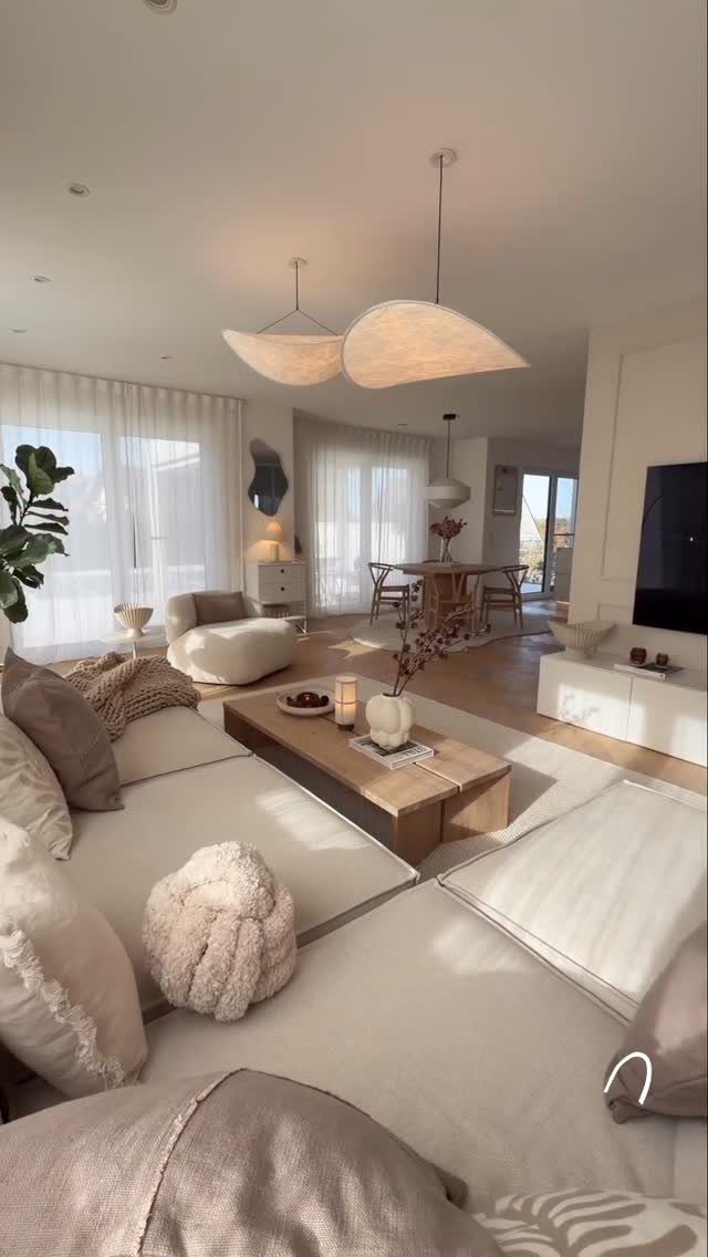 Modern minimalist living room with beige modular sofa, wooden table, and organic pendant lights.