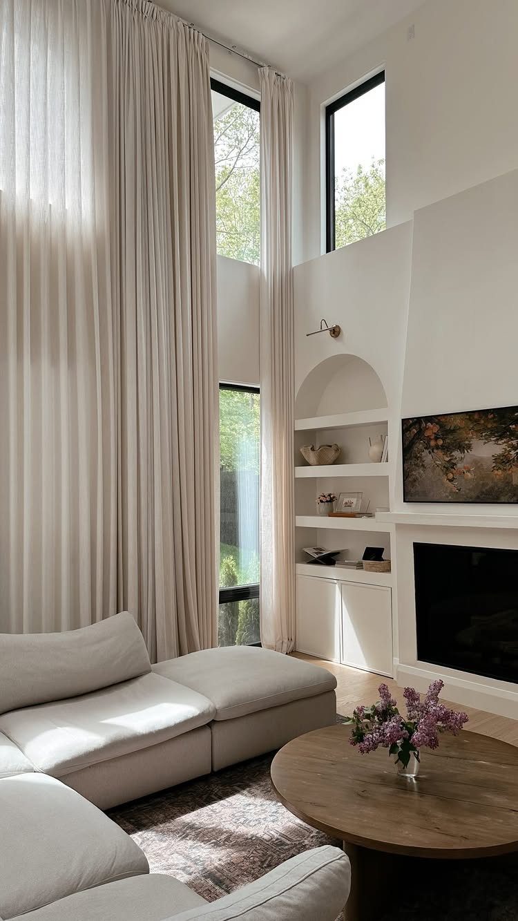White sheer curtains hanging from high ceilings in a bright, modern living room.