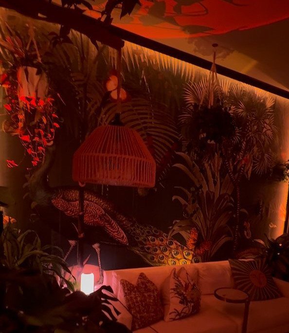Tropical living room with jungle wallpaper, wicker lamp, and white sofa with cushions.